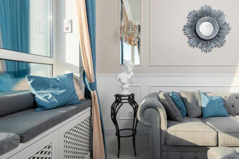 Contemporary room interior with decorative cushions on sofa under mirror on sunny day at home